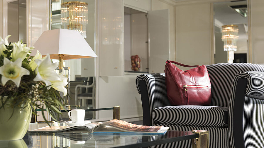 Detalle en la suite del Maritim Hotel Ulm con sillón a rayas, bolso rojo y lirios