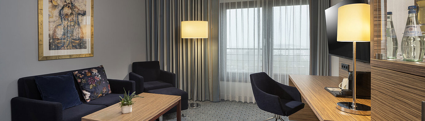 Junior suite at the Maritim Hotel Darmstadt with stylish decor, sofa, desk, TV, and large windows for ample daylight.