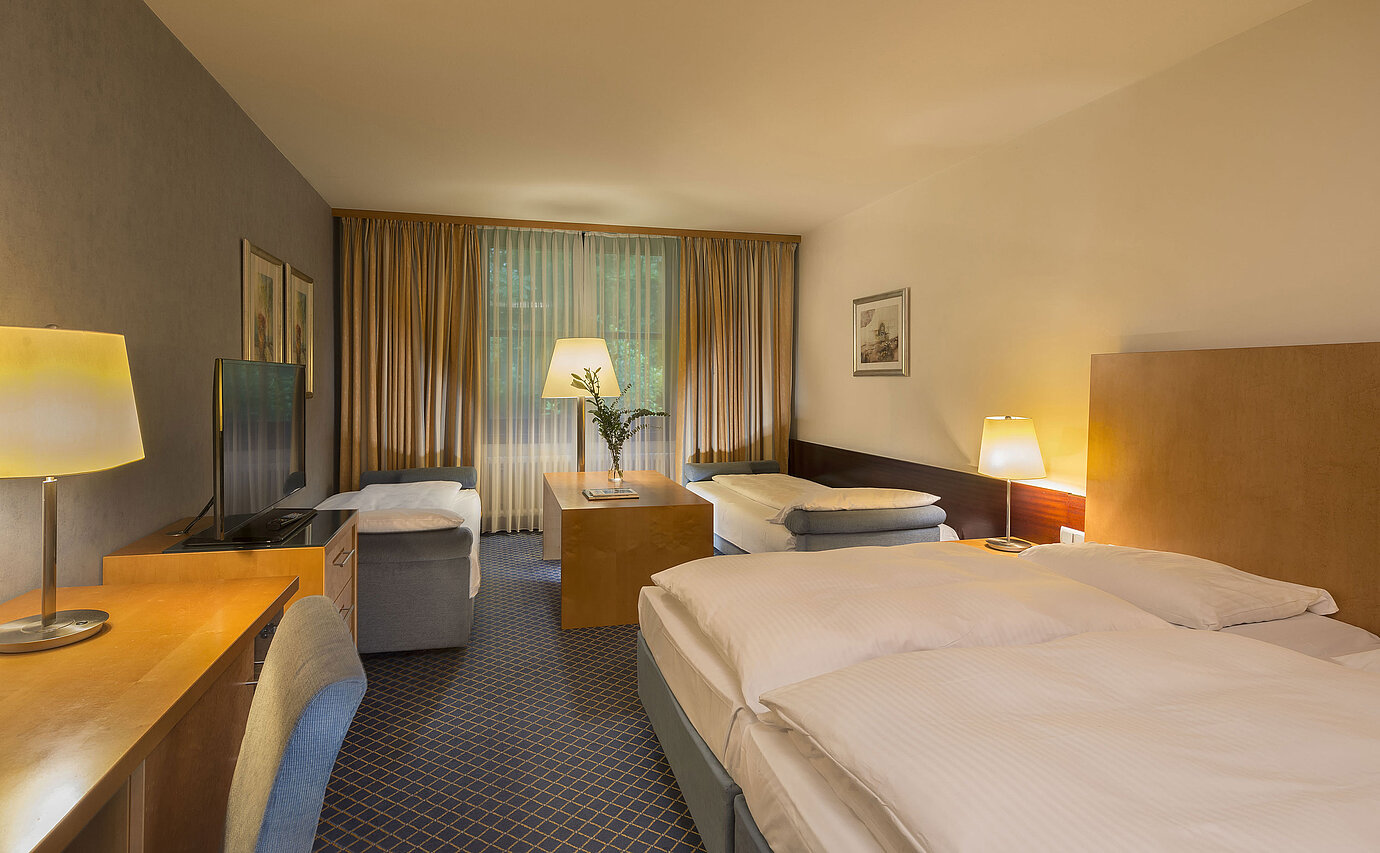 Habitación familiar espaciosa en el Maritim Hotel Fulda con cuatro camas, escritorio y ambiente acogedor.