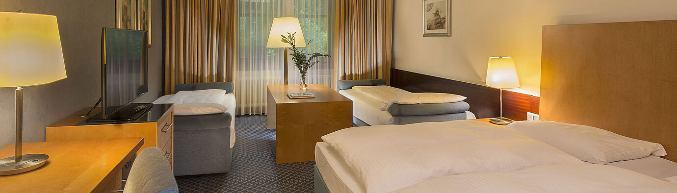 Chambre familiale spacieuse au Maritim Hotel Fulda avec quatre lits, bureau et ambiance chaleureuse.