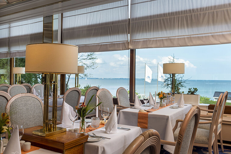 Restaurant élégant avec des tables dressées et vue sur la mer,décoré de lampes et de fleurs pour une expérience gastronomique