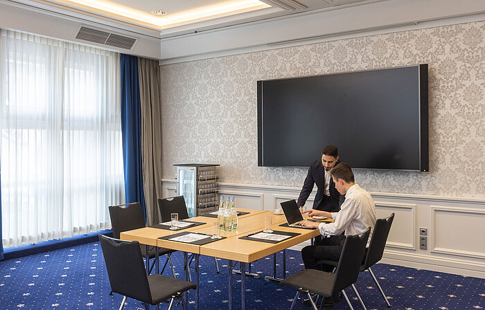 Dos personas trabajando en el Salon Oegg del Maritim Hotel Würzburg con pantalla moderna.