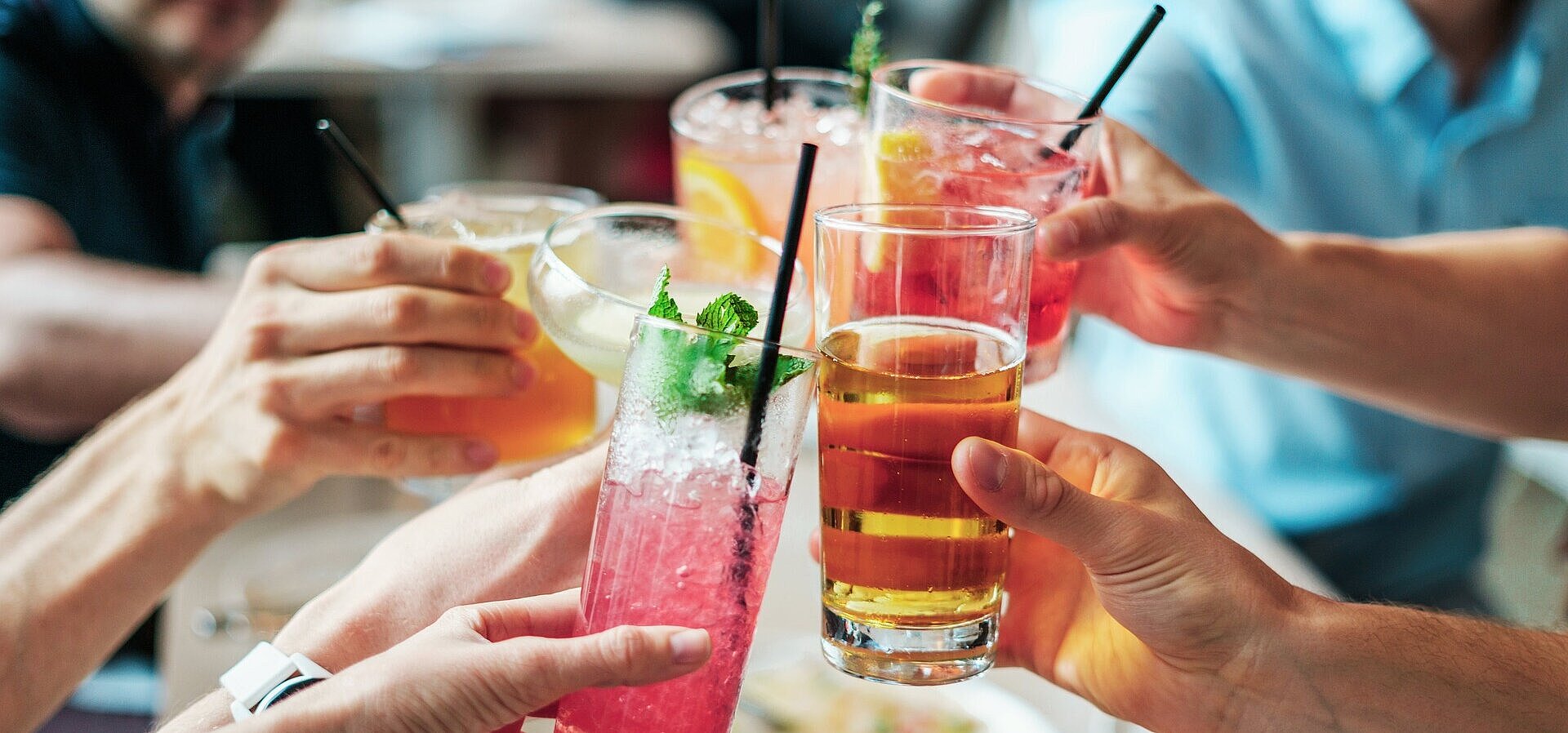 Several people clinking glasses with colourful drinks and cocktails during a social gathering.