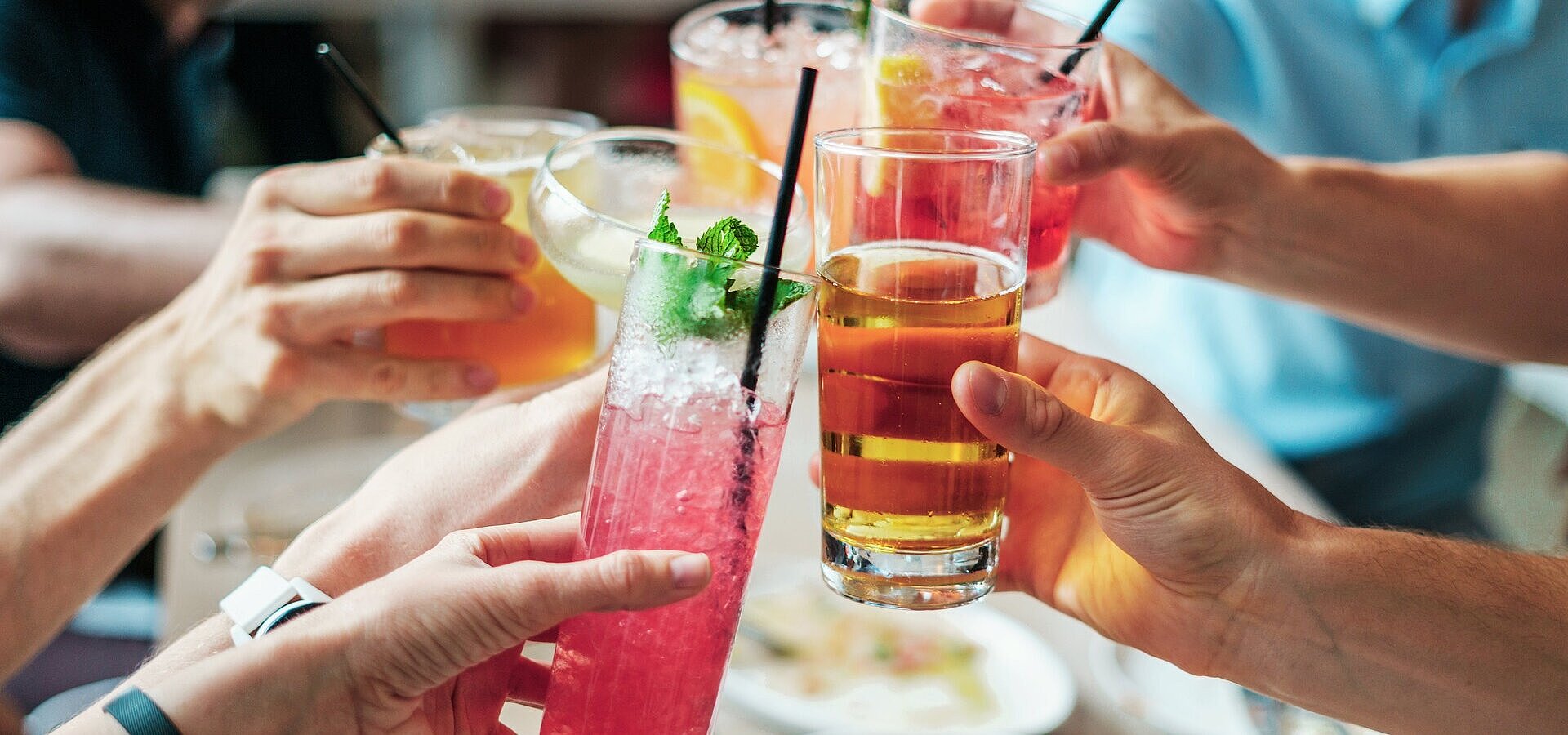 Several people clinking glasses with colourful drinks and cocktails during a social gathering.