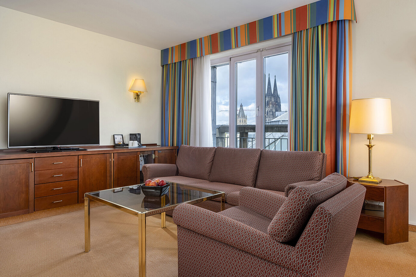 Soggiorno della Senior Suite al Maritim Hotel Köln con divano, TV e vista sul Duomo di Colonia.