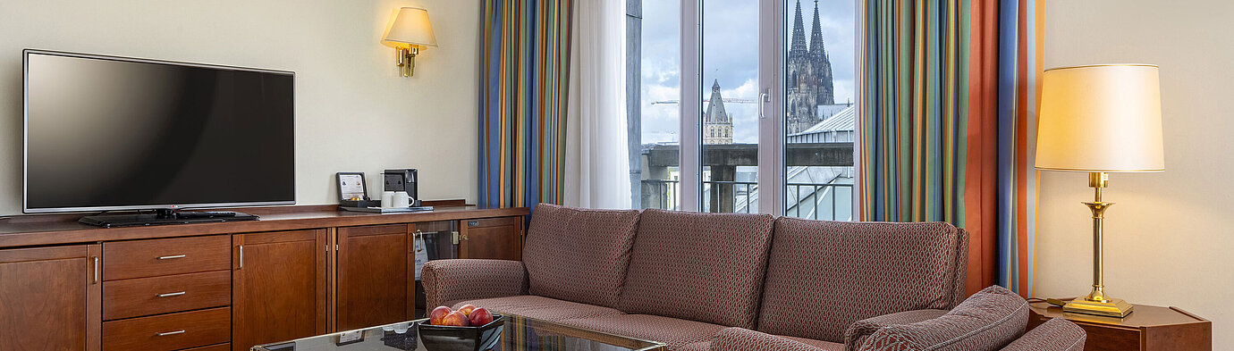 Suite Senior Salon de la Suite Senior au Maritim Hotel Köln avec canapé, télévision et vue sur la cathédrale de Cologne.