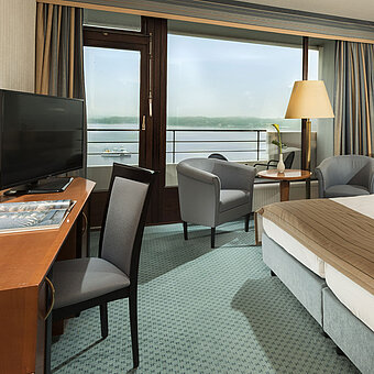Habitación superior del Maritim Hotel Kiel con escritorio, zona de estar, cama doble grande y balcón con vistas al fiordo.