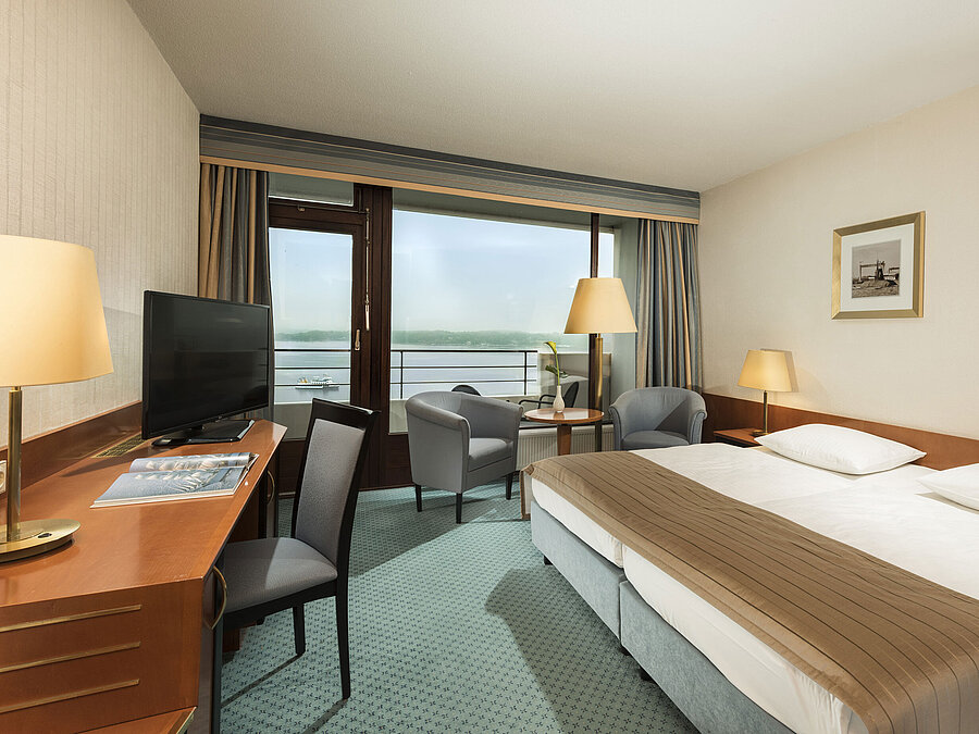 Superior room at the Maritim Hotel Kiel with desk, seating area, large double bed and balcony overlooking the fjord.