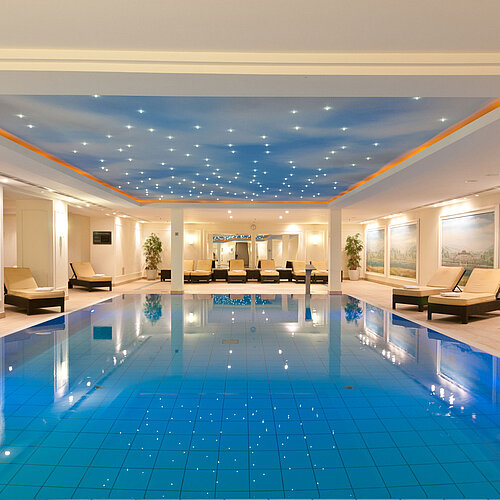 Piscina cubierta lujosa en el Maritim Hotel Dresden con tumbonas y iluminación ambiental en el techo.