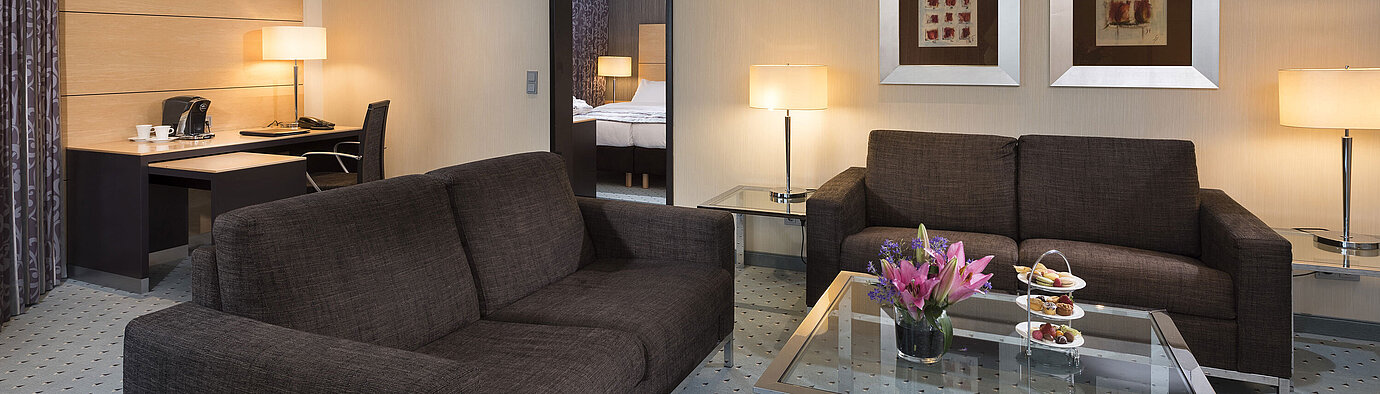 Suite Junior à l’hôtel Maritim Düsseldorf avec salon séparé, deux canapés, bureau, fleurs et design moderne.