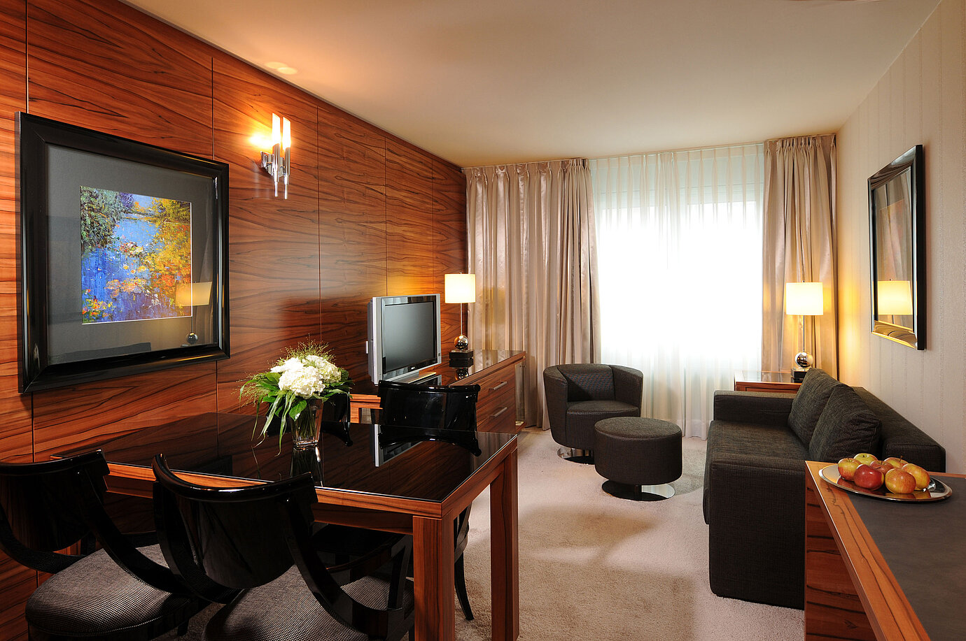 Zona soggiorno luminosa con divano, poltrona, TV e scrivania al Maritim Hotel Monaco