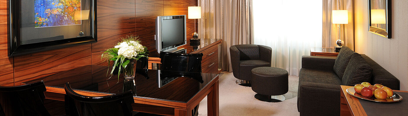 Espace salon lumineux avec canapé, fauteuil, TV et bureau à l’hôtel Maritim Munich