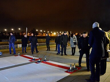 Guests playing Bavarian curling on a lit rooftop terrace at night with city views.