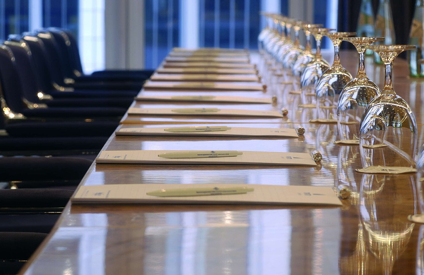 Primer plano de una mesa de conferencia preparada en el hotel Maritim proArte Berlín, con blocs de notas y copas de vino.