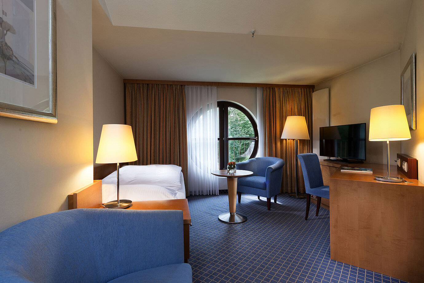 Habitación Classic en Maritim Hotel Fulda con cama individual, escritorio, zona de estar y ventana redonda con vistas.