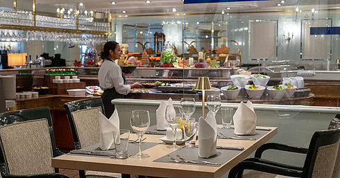 Restaurant area with set table, buffet station in the background and a staff member at Maritim Hotel.