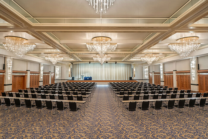 Fürst-von-Metternich Hall with large stage, row seating, elegant chandeliers and bright interior.