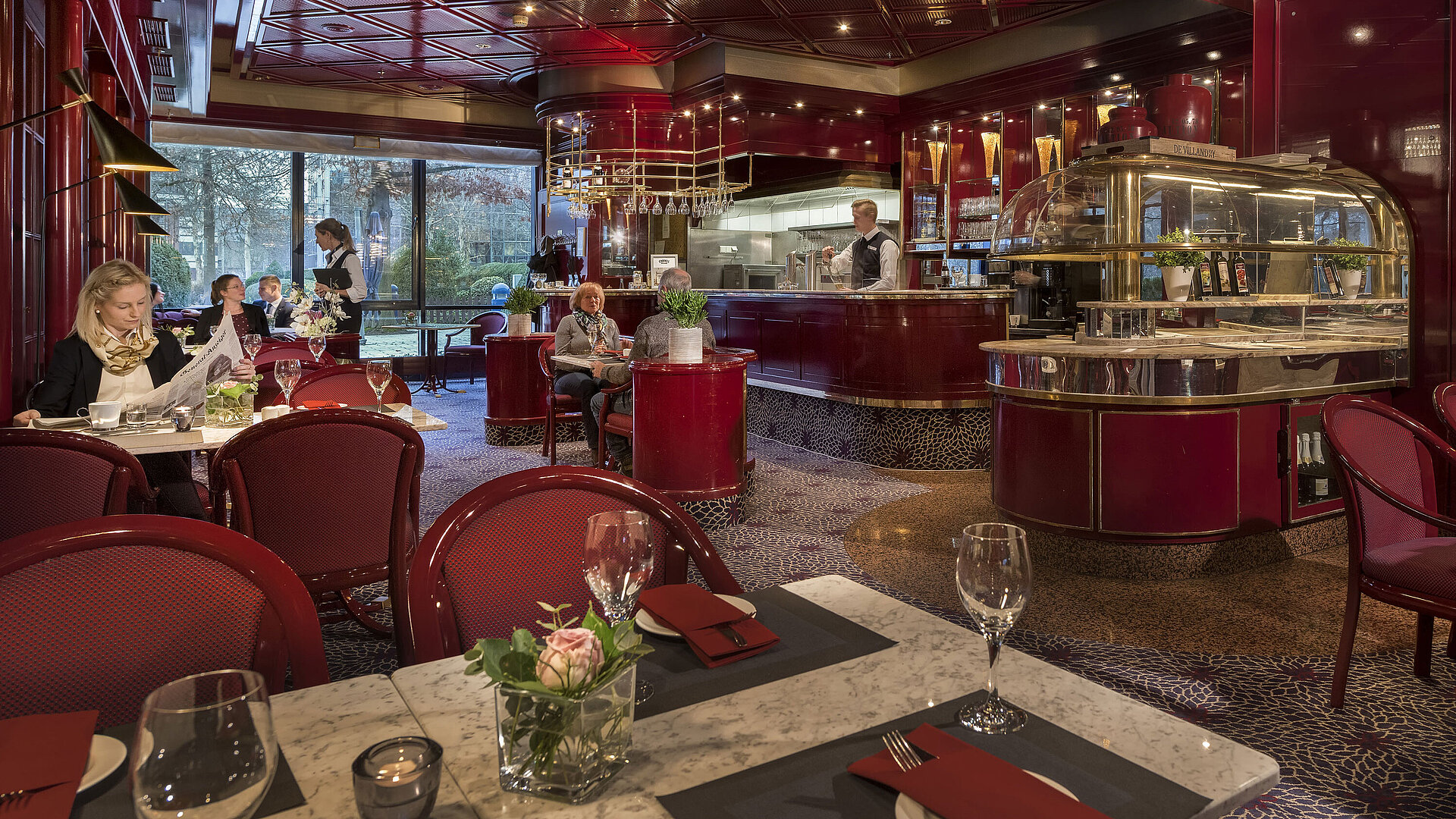 The image shows the cozy "Brasserie" café at the Maritim Hotel Bonn with red decor and a relaxed atmosphere.