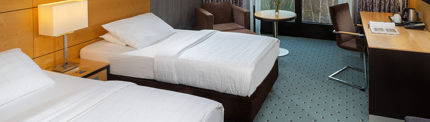 Chambre classique au Maritim Hotel Düsseldorf avec deux lits simples, bureau, fauteuil et fenêtre avec vue sur l'aéroport.