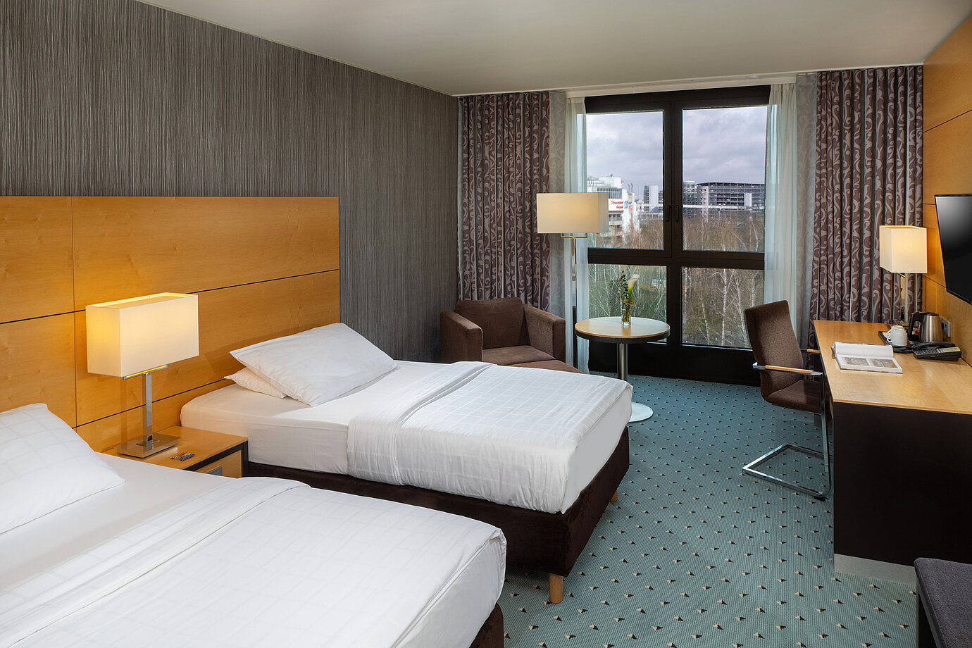 Chambre classique au Maritim Hotel Düsseldorf avec deux lits simples, bureau, fauteuil et fenêtre avec vue sur l'aéroport.