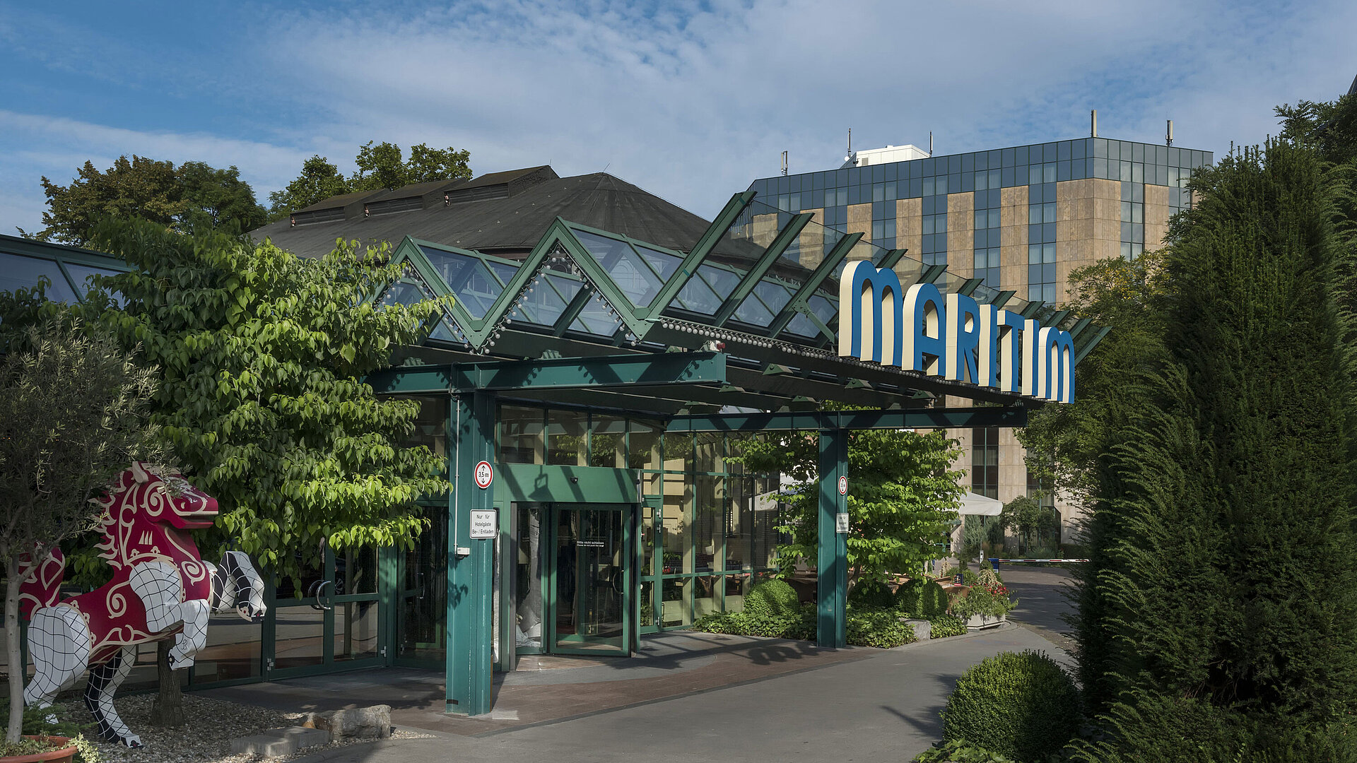 Main entrance of Maritim Hotel Stuttgart with glass roof, green facade and Maritim logo