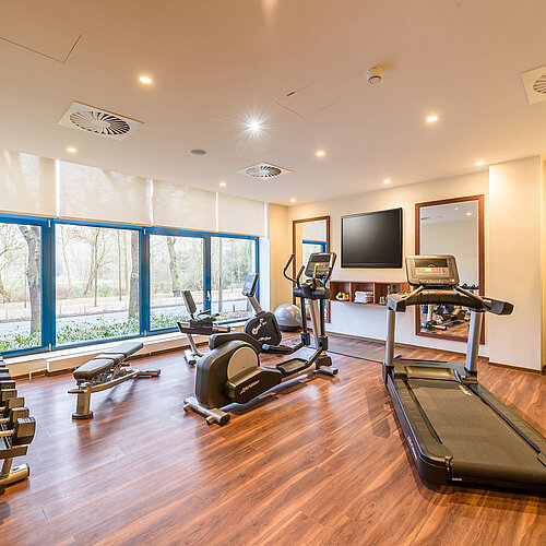 Salle de fitness moderne avec vue à l'hôtel Maritim Bremen, équipée de tapis de course, haltères et machines.