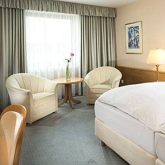 Habitación luminosa con dos camas, zona de estar y ventana grande en el Maritim Hotel Magdeburg