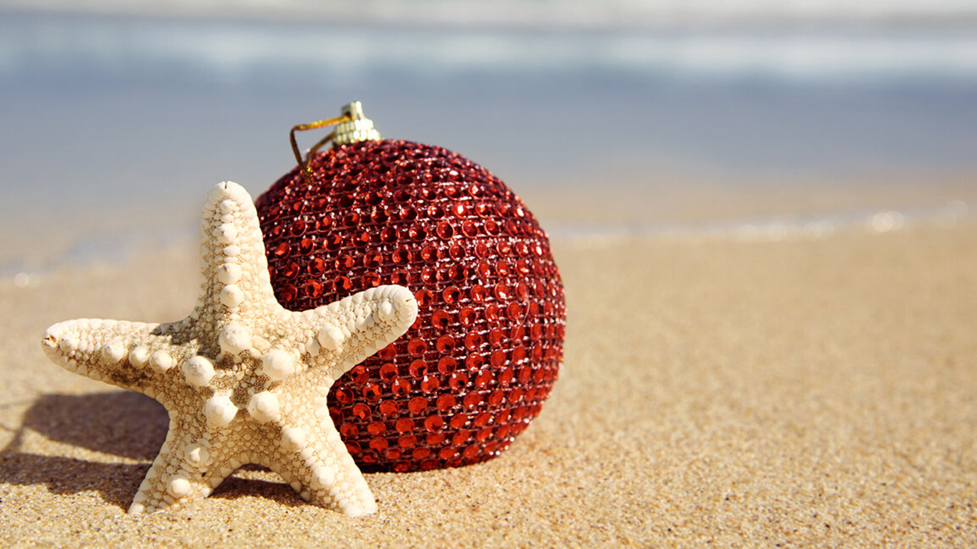 Red Christmas bauble with star motif placed in the sand – festive beach vibes with a holiday feeling