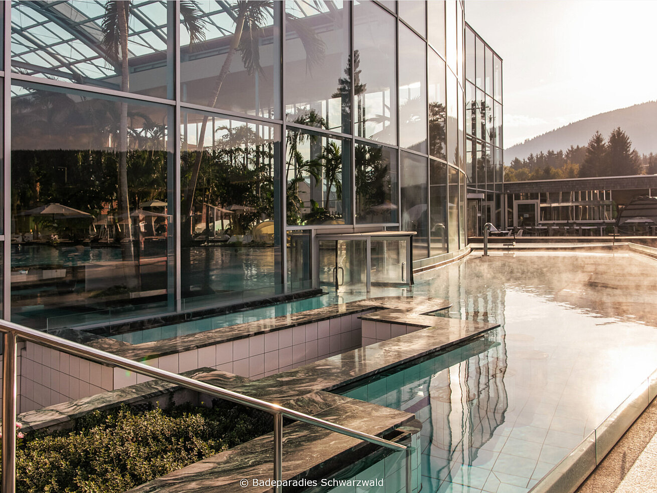 Modern spa building with outdoor pool and water features at sunset