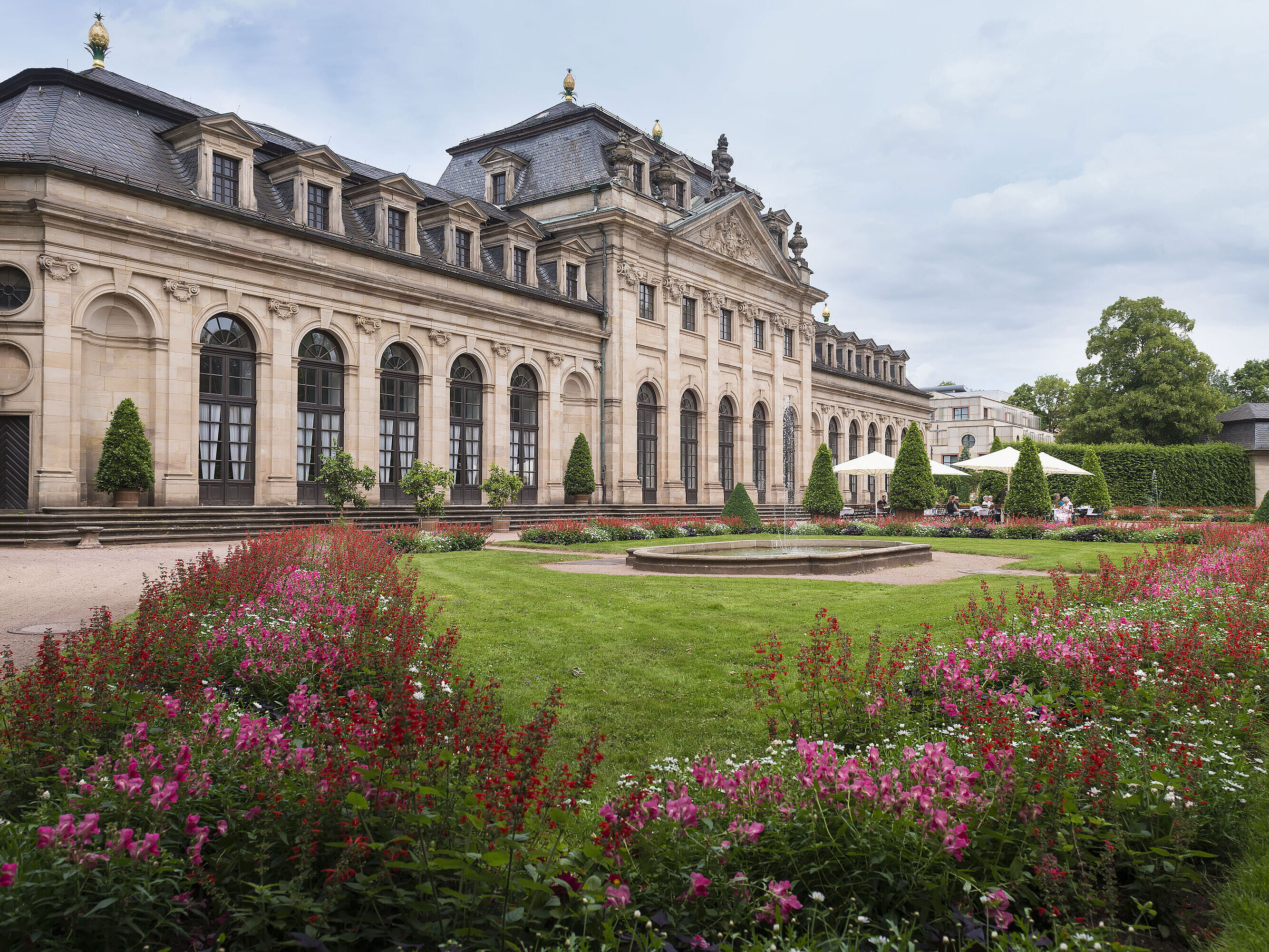 La histórica Orangerie de Fulda con fachada barroca, escalinata y jardín en flor en primer plano.