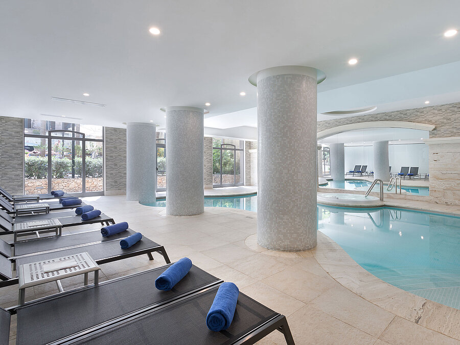 Modern indoor pool with sun loungers and towels at the spa of Maritim Antonine Hotel & Spa Malta for relaxing wellness moments.