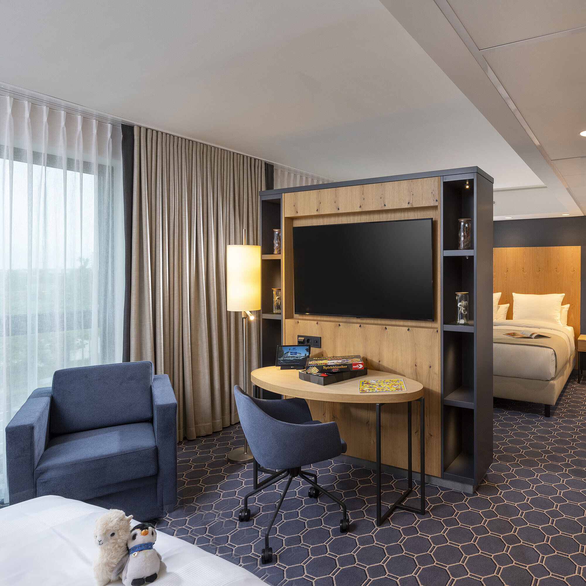 Suite familiale Chambre lumineuse au Maritim Hotel Ingolstadt avec coin salon, bureau, grand téléviseur et vue sur la verdure.