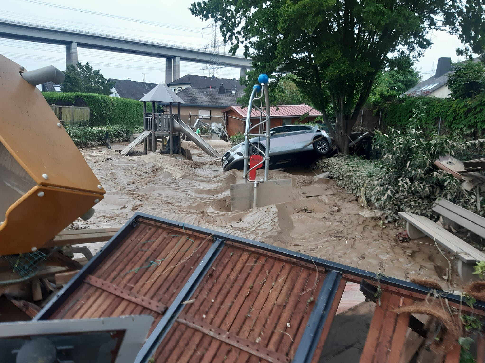 Daños por inundación en un parque infantil Parque infantil inundado con un coche dañado y barro tras una inundación en una zona residencial