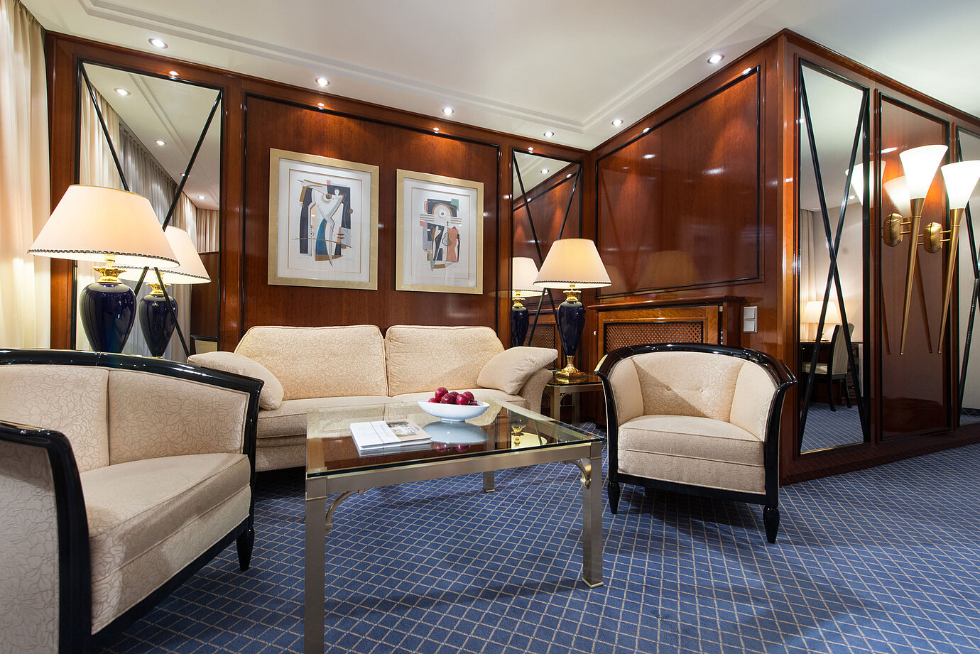 Elegante sala de estar de una suite en Maritim Hotel Fulda con muebles sofisticados, mesa de vidrio e iluminación acogedora.