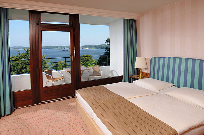 Suite Junior Junior Suite en el Maritim Hotel Kiel, cama doble, balcón con asientos y vistas al fiordo de Kiel.