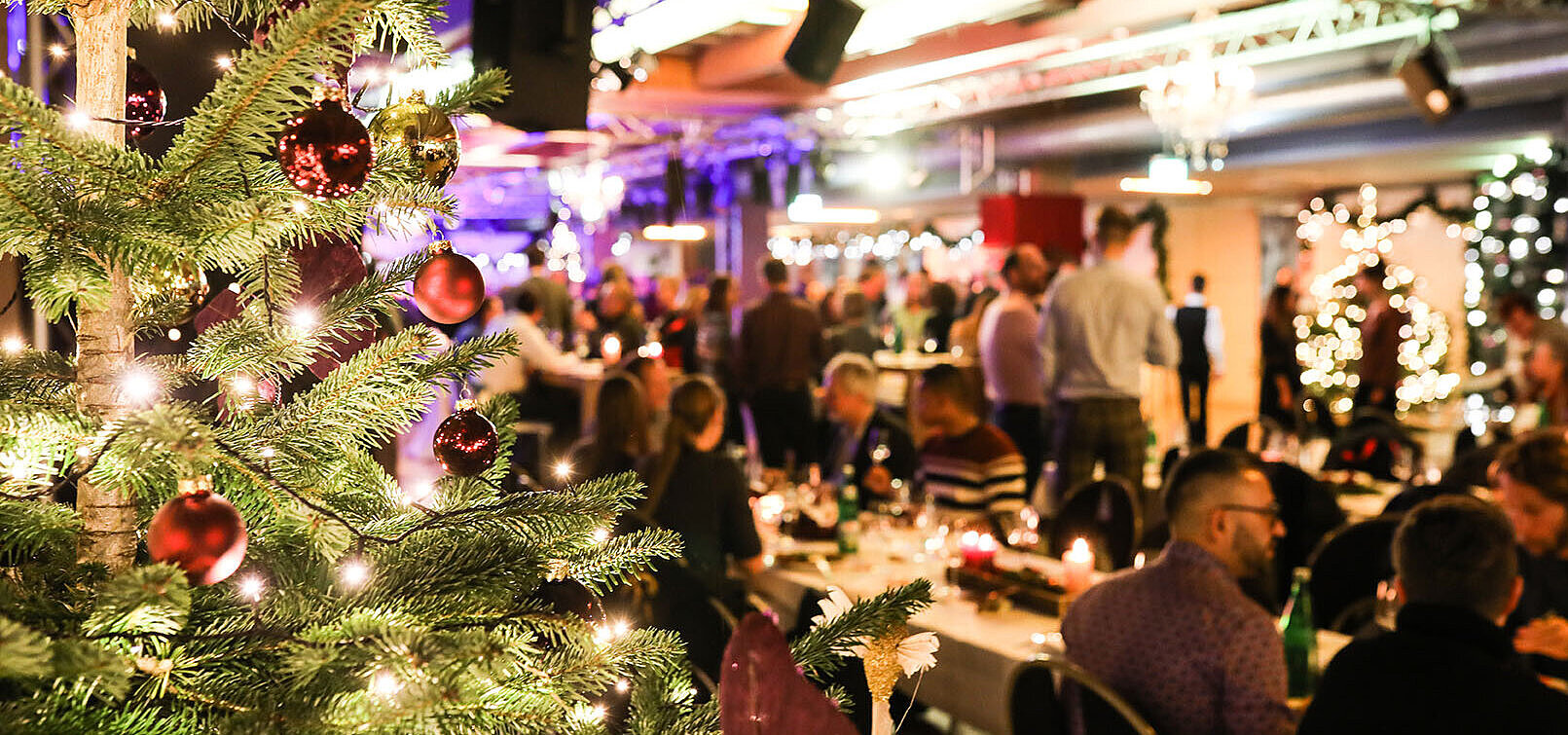 © bilderstöckchen - AdobeStock.com Christmas party with decorated tree and guests in a festive hall