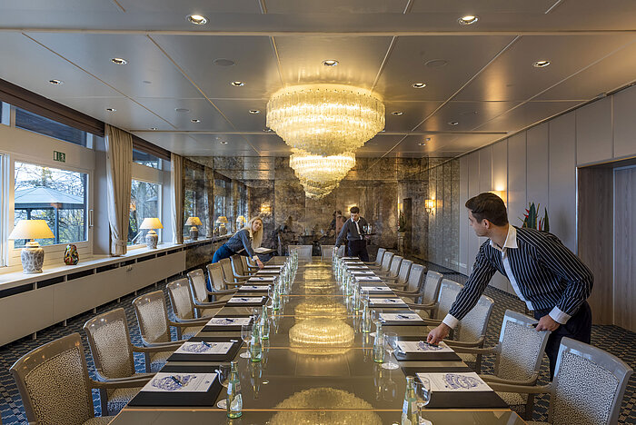 Salón Oslo en el Maritim Hotel Kiel, elegante sala de conferencias con lámparas de araña y una larga hilera de mesas, personal preparando la sala.