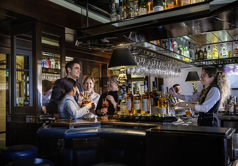 Des clients profitent de cocktails et d'une ambiance chaleureuse au bar de l'hôtel Maritim Darmstadt.