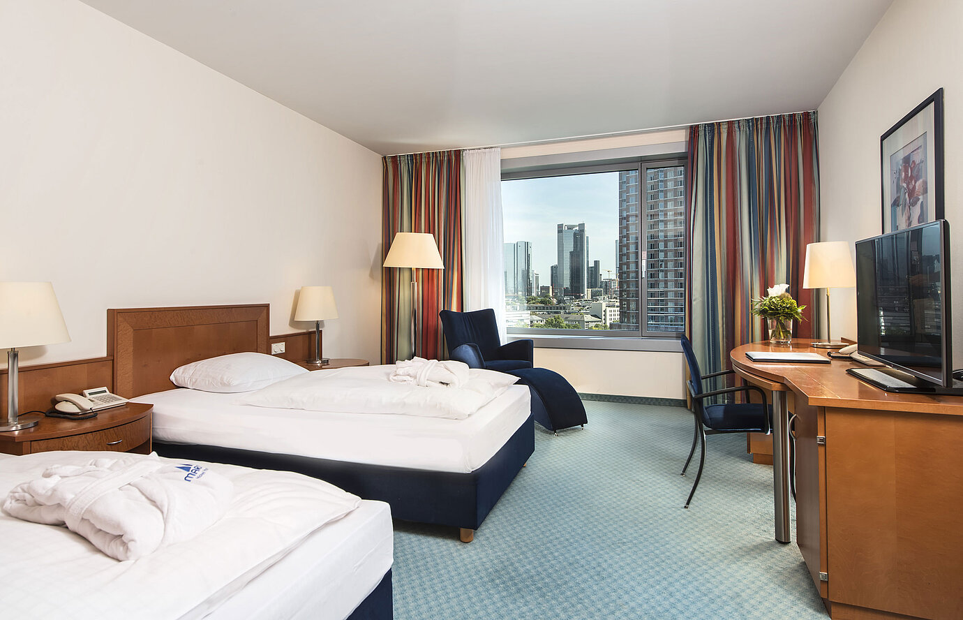 Camera superior al Maritim Hotel Frankfurt con due letti singoli, scrivania, area salotto e splendida vista sulla skyline.