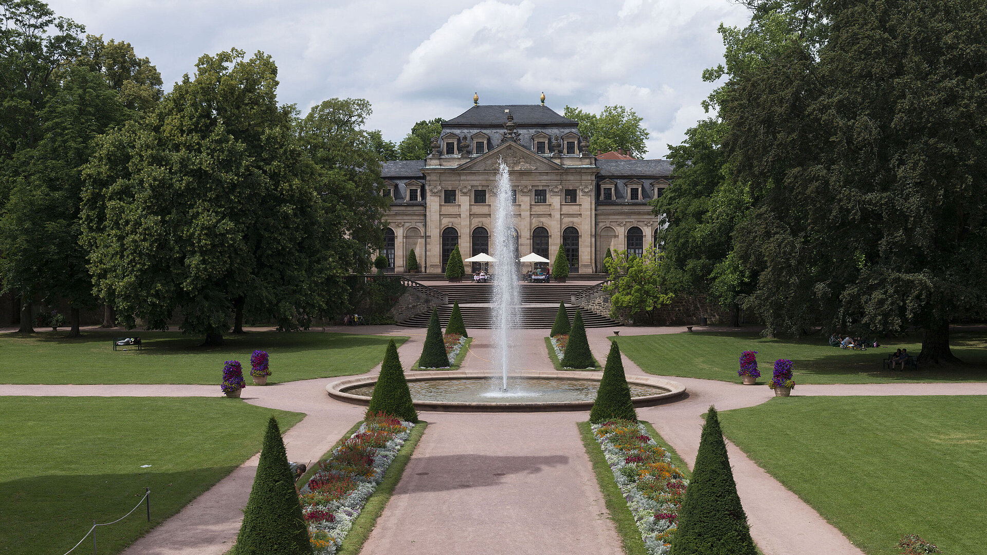 Vista exterior La Orangerie barroca de Fulda con jardín del palacio, fuente y coloridos parterres de flores.