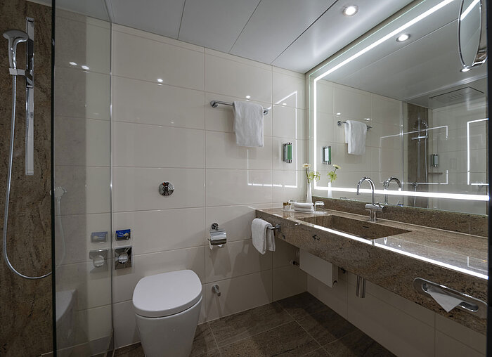 Salle de bain moderne à l'hôtel Maritim Bremen avec équipements luxueux, grand miroir éclairé et douche à l'italienne.