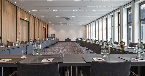 Salle de réunion de l'hôtel Maritim Ingolstadt avec grandes fenêtres, sièges en U et matériel de conférence.