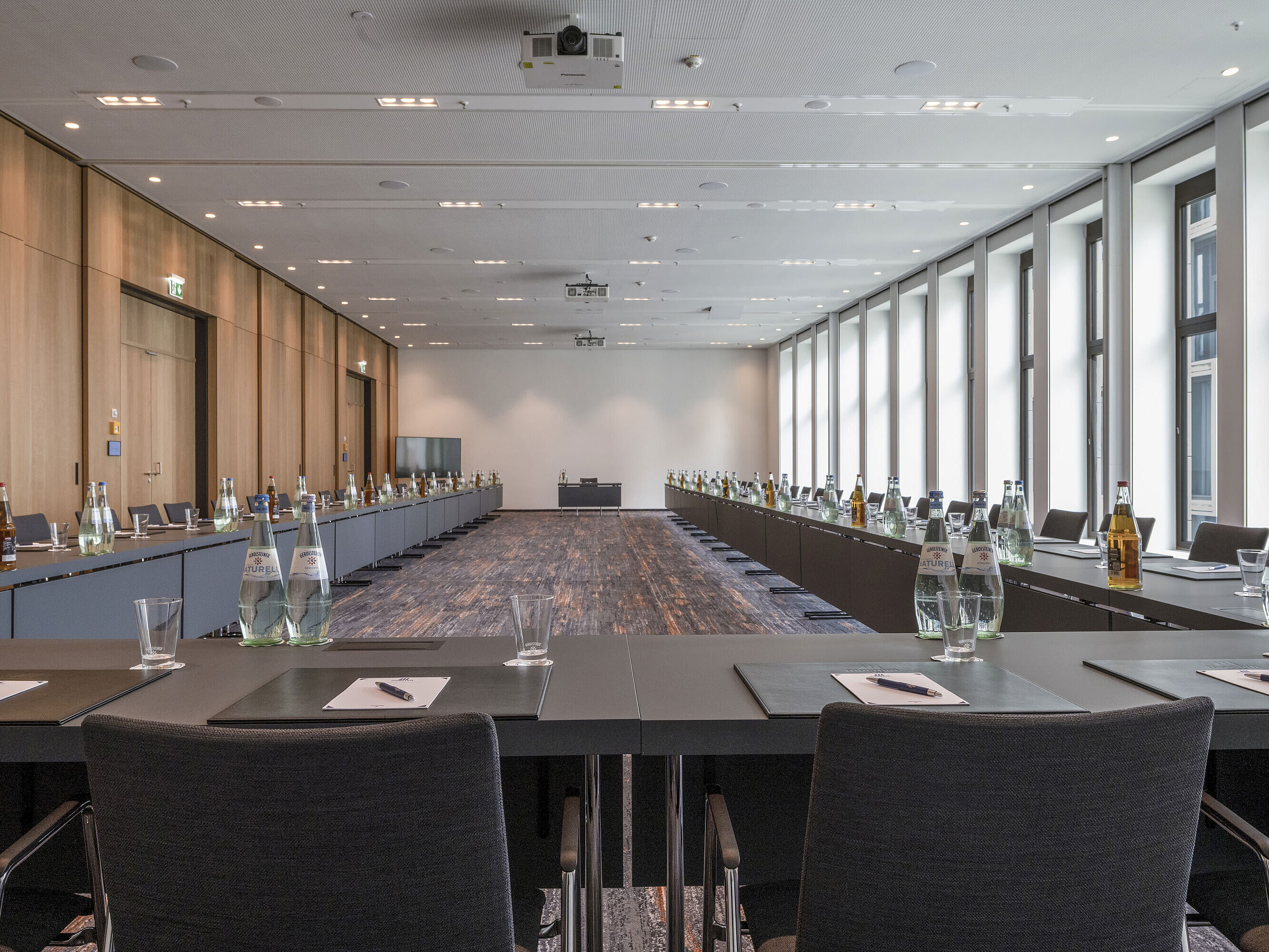 Salle de réunion de l'hôtel Maritim Ingolstadt avec grandes fenêtres, sièges en U et matériel de conférence.