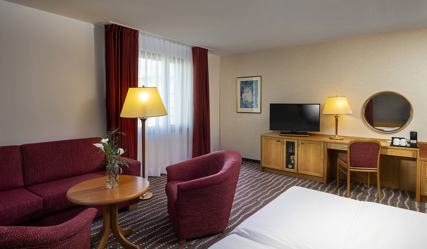 Studio confortable au Maritim Hotel Magdeburg avec coin salon, bureau et télévision moderne.