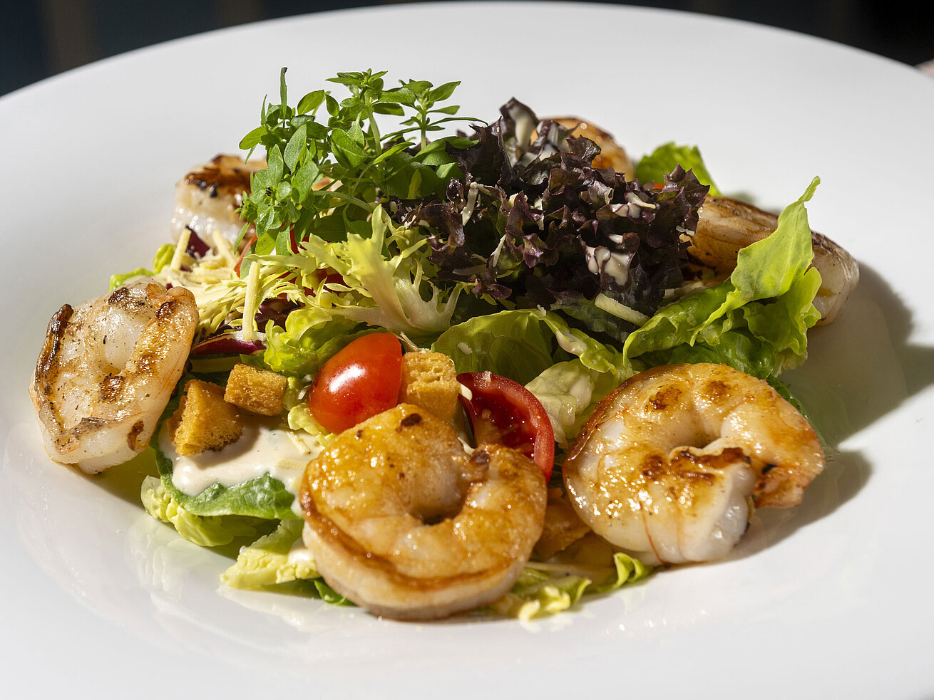 Pan-fried prawns served on fresh leaf salad with cherry tomatoes and Mediterranean accompaniments.