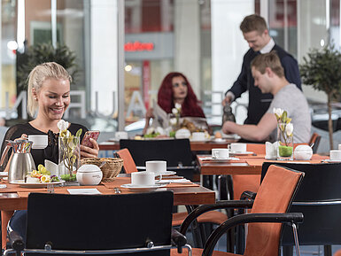 Les hôtes profitent du petit-déjeuner au restaurant. Une ambiance conviviale avec un service et des plats frais.