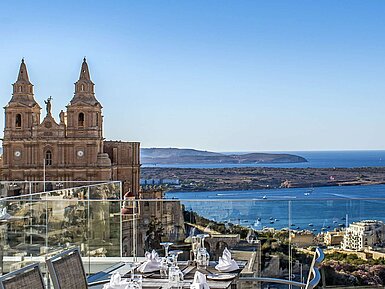 Ristorante panoramico con tavoli apparecchiati e vista su chiesa, costa e mare
