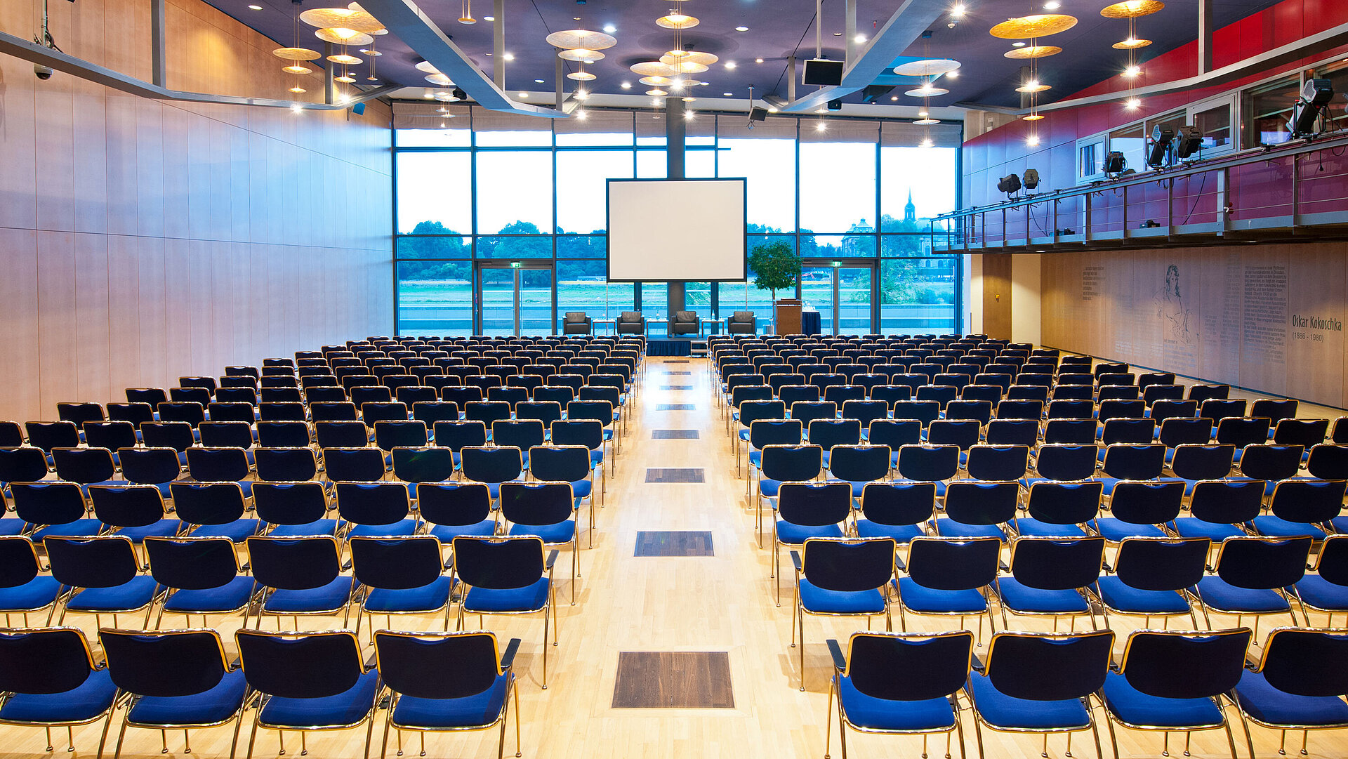 Gran sala de conferencias del Maritim Hotel Dresde con filas de sillas azules y vista al río Elba.
