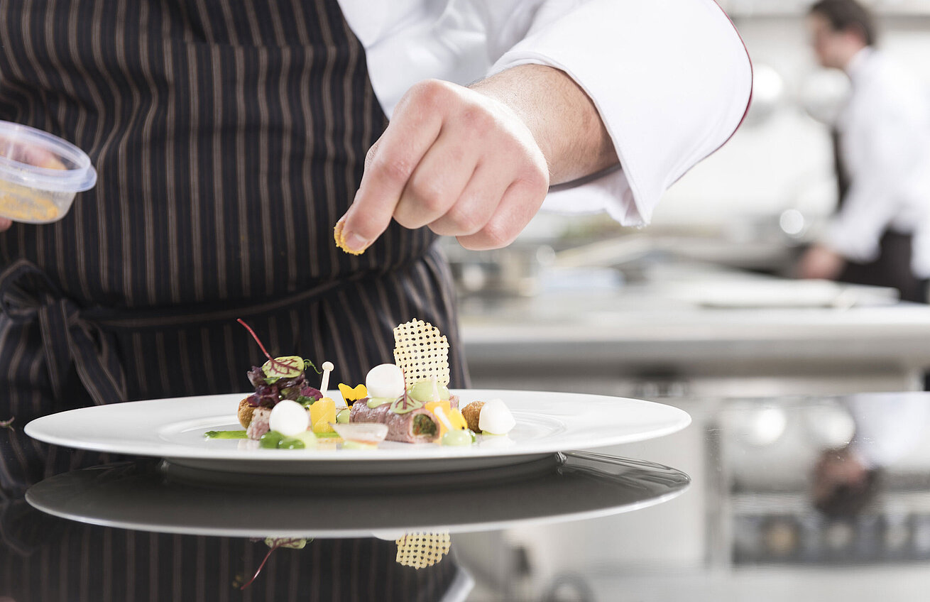  Chef plating a gourmet dish with vegetables, herbs, and artistic elements at the Orangerie.