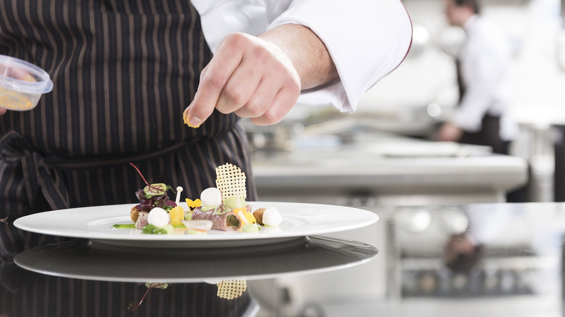  Chef plating a gourmet dish with vegetables, herbs, and artistic elements at the Orangerie.